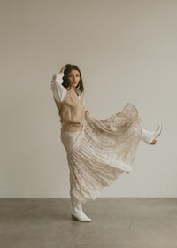 a woman in a beige skirt is dancing in a white room