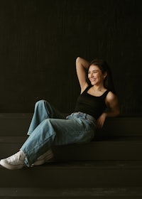 a young woman in jeans and a black tank top sitting on steps