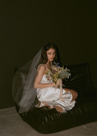 a bride sitting on a black couch holding a bouquet